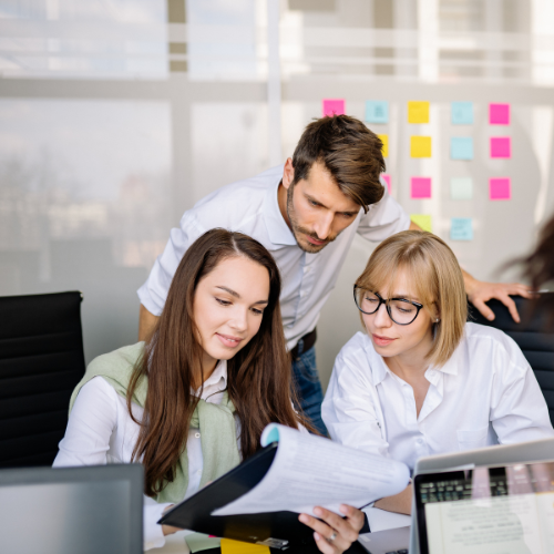 Three people in an office inspect a clipboard